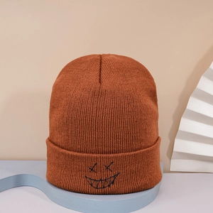 Detail of a brown knit beanie featuring a black embroidered devil smile face design