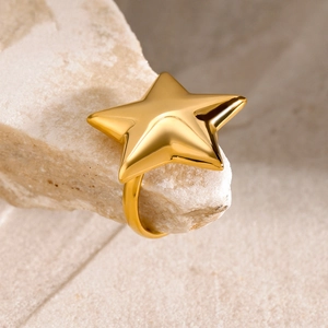 Macro shot of 18k gold star ring on a textured stone base with mirror finish reflection