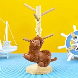 Close-up of a cute brown plush camel keychain hanging on a wooden display stand.