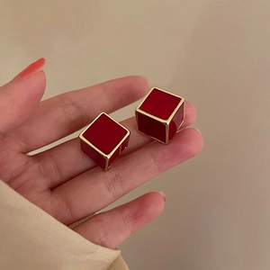 Detail of red cubic tulip stud earrings with gold trim held between fingers