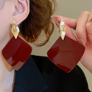 Detailed close-up of large geometric drop earrings with gold rhombus and red square charms