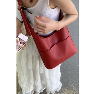 Detail of red litchi texture PU leather hobo bag with gold hardware on a white dress