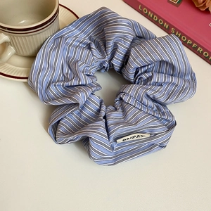 Detail of blue striped cotton scrunchie with woven label next to a coffee cup