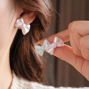 Close-up of pink and light blue pearlescent bow stud earrings on a model ear