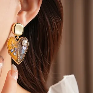 Vintage gold heart earrings with resin and pearls shown on a model in a warm-toned closeup