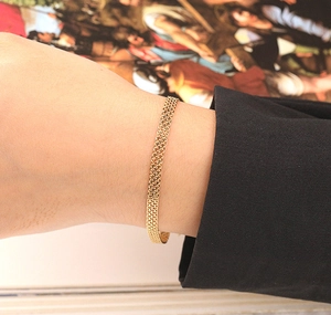 Detailed view of a gold-plated woven mesh bracelet styled on a person's wrist