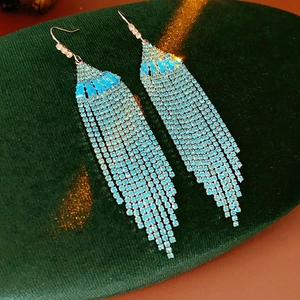 Detailed macro of long blue rhinestone tassel earrings on a green velvet base