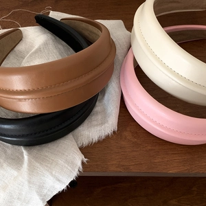 Padded leather headbands for women in assorted colors on a minimalist wooden surface