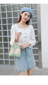 Detail of light green PU leather and straw bucket bag with drawstring closure on a model