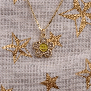 Detailed close-up of a gold flower necklace with a yellow enamel smiley face and zircon