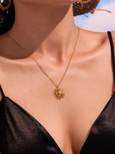 Detail of gold sun goddess pendant necklace worn by model against a blue sky background