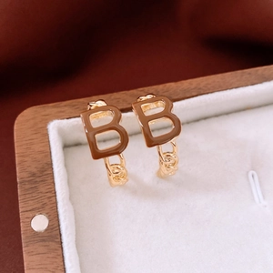 Close-up of gold-plated B-letter C-shaped earrings with brown enamel in a wooden box