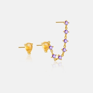 Detail of asymmetrical gold earrings featuring a yellow teardrop gem and purple stones
