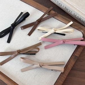 Set of six vintage leather bow hair clips in assorted earth tones on a wooden tray