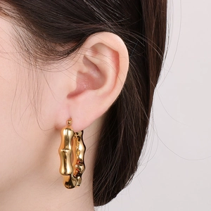 Detail shot of a model wearing chunky gold bamboo-textured hoop earrings in stainless steel