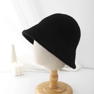 Detail view of the black knitted bucket hat showing the soft texture on a wooden head stand