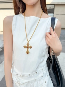 Gros plan d'un collier croix vintage avec pierres rouges porté par un mannequin