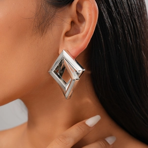 Close-up of a large silver geometric diamond-shaped earring on a model's ear