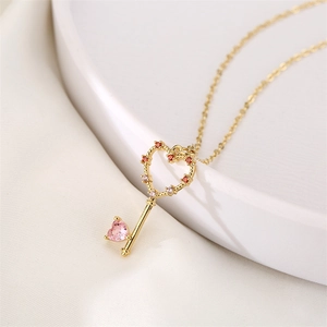Gold heart key necklace with pink zircon pendant displayed on a white ceramic plate