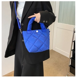 Close-up of bright blue quilted crossbody bag with rhombic pattern and round buckle