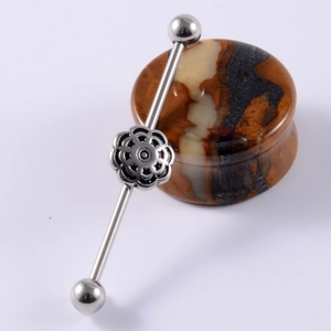 Detailed close-up of a stainless steel industrial barbell earring with a floral center piece