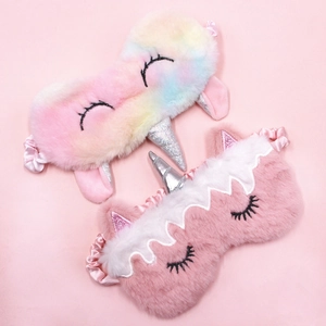 Rainbow and pink plush unicorn sleeping masks with silver horns on pink background
