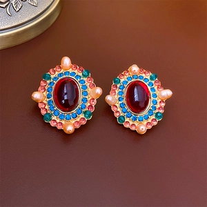 Vintage gold earrings with large red oval gem, blue stones, and pearls on leather background