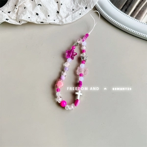 Detail of pink beaded phone strap featuring bear, star and heart charms on a white surface