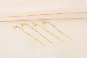 Detailed view of four golden S925 silver star and moon tassel long ear wires on beige fabric