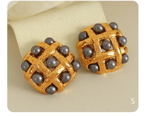 Macro shot of gold-plated woven texture earrings featuring dark grey pearl studs