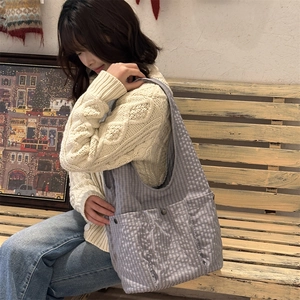 Detail view of grey plaid tote bag with front pockets and black metal buckle on a bench