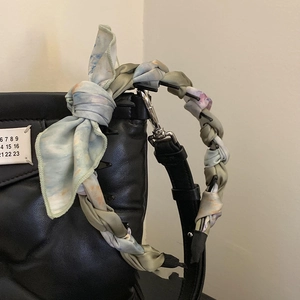 Close-up of black quilted leather handbag handle wrapped with colorful silk twilly scarf