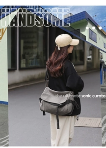 Gray canvas messenger bag worn by a model in a stylish urban street scene close-up