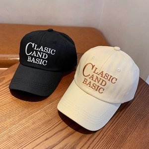 Detail of classic embroidered letters on black and cream baseball caps on wood table