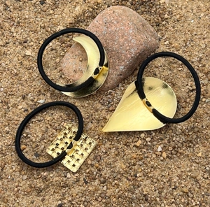 Close-up of gold crescent and teardrop metal hair ties on natural stone background