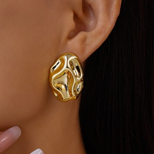 Detailed view of gold earrings with irregular hammered texture and liquid metal finish