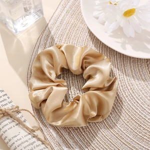Detail of champagne gold satin scrunchie showing silky texture and elegant folds
