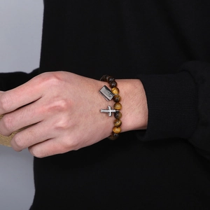 Makroansicht von Tigerauge-Armband mit Freimaurerkreuz und Buchanhänger am Handgelenk