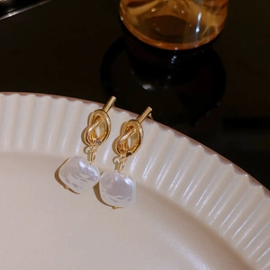 Detail of gold metal knot earrings with irregular white pearl drops on a ceramic plate