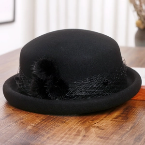 Close-up of black wool felt beret with elegant mesh veil and two plush pompom details