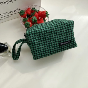Detail of green and black houndstooth pattern bag with hand strap and woven brand label