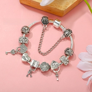 Detailed macro of a silver snake chain bracelet featuring heart charms and key pendant