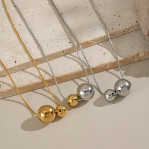 Three geometric double ball necklaces in gold and silver finishes on stone steps