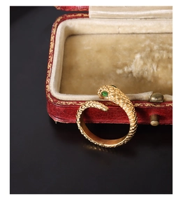 Detail of 18k gold plated snake ring with green gemstone eyes and scale texture