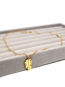 Macro shot of a golden leaf pendant on a chain resting in a gray velvet jewelry box