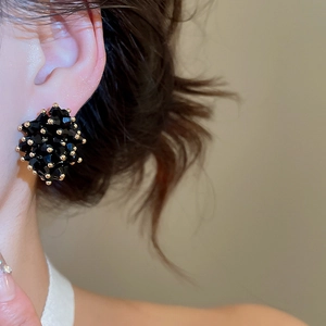Close-up of irregular black crystal cluster stud earrings with gold accents on model