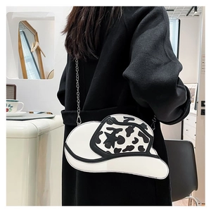 Detail of cowboy hat shaped crossbody bag with black and white cow print and chain strap