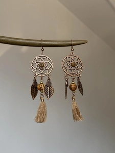 Détail de boucles d'oreilles bohèmes attrape-rêves avec perles en bois et pompons beiges