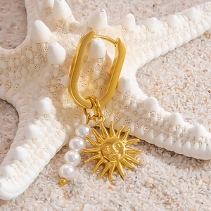 U-shaped gold earrings with sun pendant and pearls displayed on white starfish