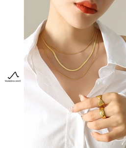 Detail of a woman wearing triple-layered gold stainless steel necklaces and matching rings